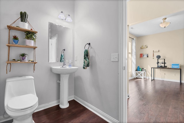 half bath with toilet, wood finished floors, and baseboards
