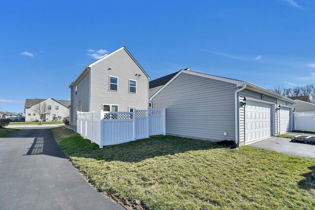view of side of home featuring aphalt driveway, fence, and a yard