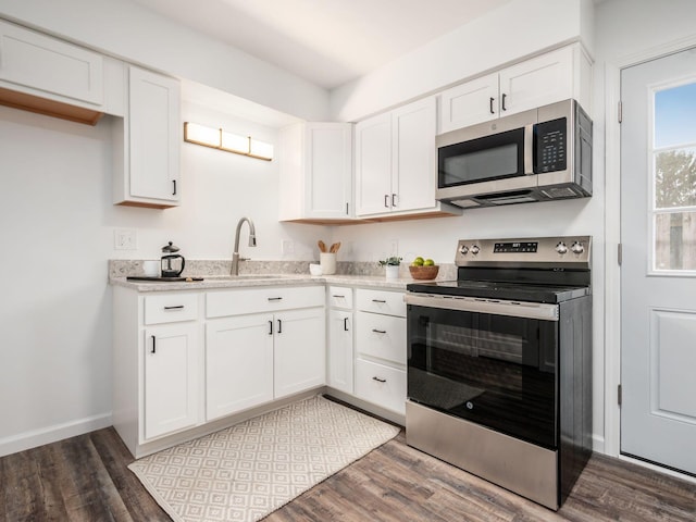 kitchen featuring white cabinetry, stainless steel appliances, dark wood-type flooring, and baseboards
