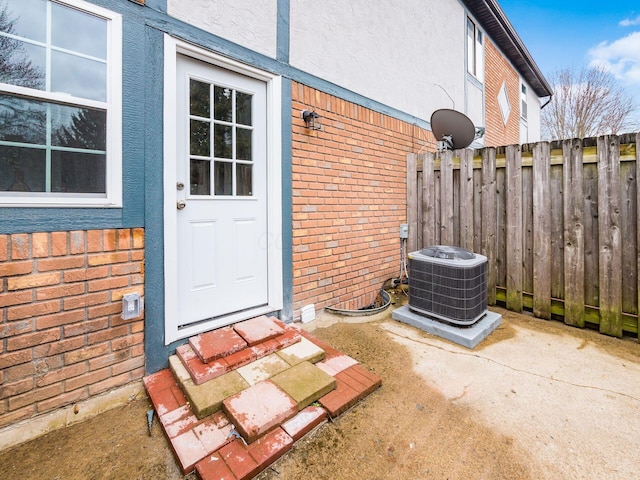 entrance to property featuring stucco siding, brick siding, central AC unit, and fence