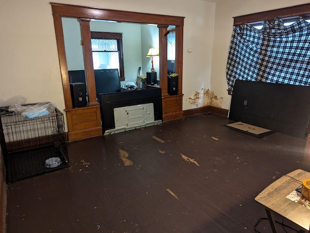 living area with baseboards, wood-type flooring, and decorative columns