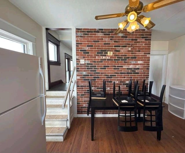 dining area featuring ceiling fan, baseboards, wood finished floors, and brick wall