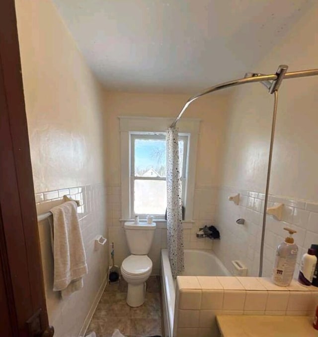 full bath featuring toilet, tile walls, and shower / tub combo with curtain