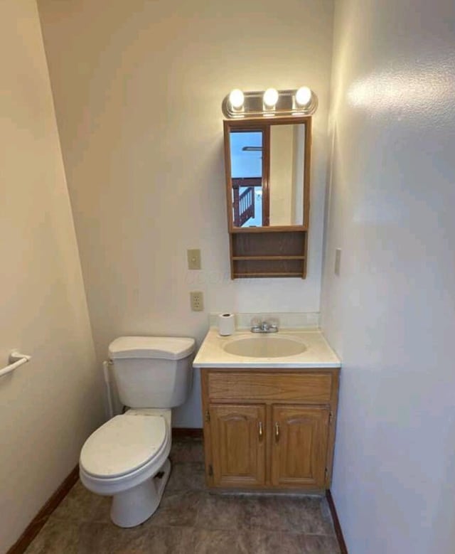 half bath with baseboards, toilet, and vanity