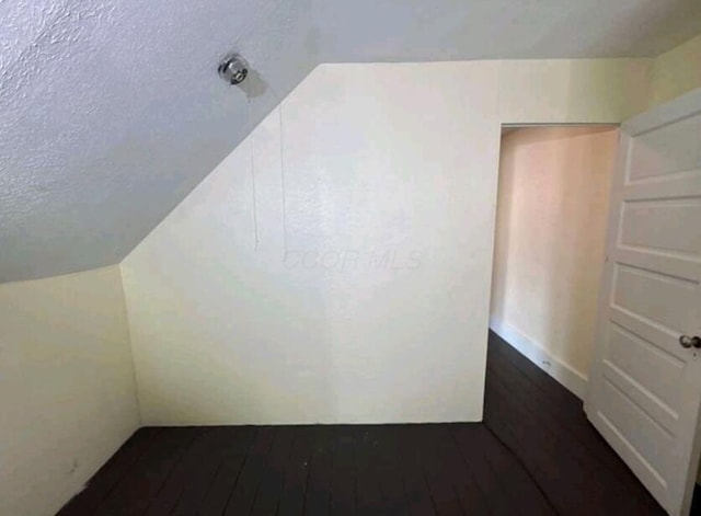 bonus room with a textured ceiling, dark wood-style floors, and vaulted ceiling