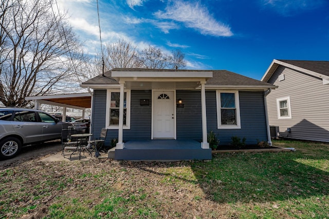 bungalow-style house featuring central air condition unit, covered porch, a front yard, a shingled roof, and a carport