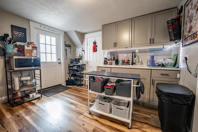 kitchen with stainless steel microwave, gray cabinetry, decorative backsplash, light wood-style floors, and a sink
