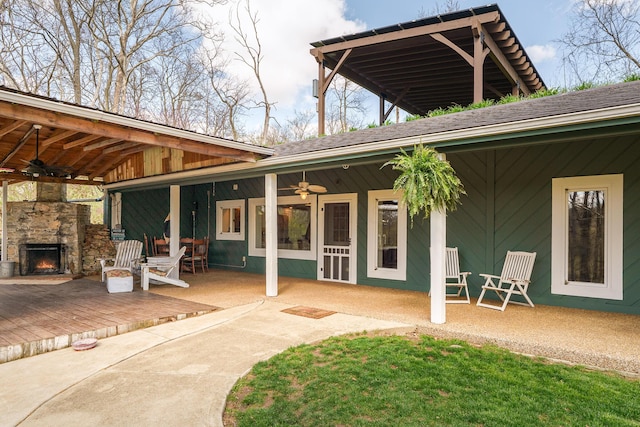 back of property with an outdoor stone fireplace, ceiling fan, a patio, and a shingled roof