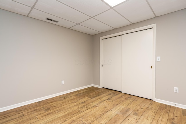 unfurnished bedroom with light wood finished floors, a closet, visible vents, baseboards, and a drop ceiling