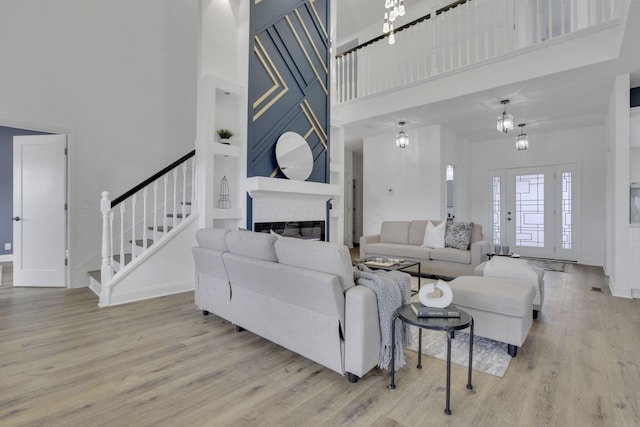 living room with stairway, baseboards, a high ceiling, light wood finished floors, and a glass covered fireplace