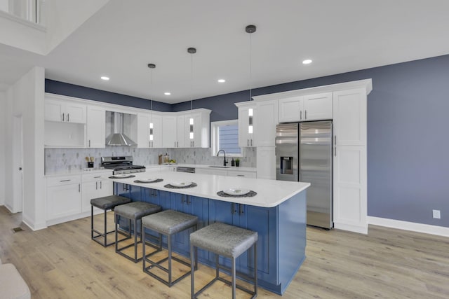 kitchen featuring light countertops, a kitchen island, a sink, appliances with stainless steel finishes, and wall chimney exhaust hood