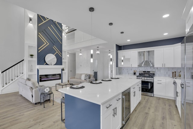 kitchen featuring stainless steel range oven, wall chimney range hood, light wood-style floors, and beverage cooler