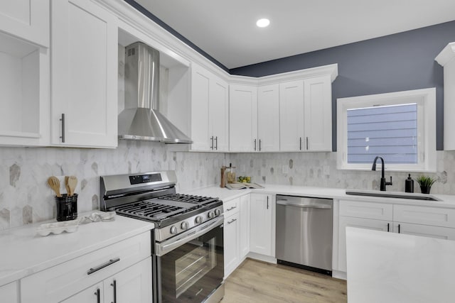 kitchen with light countertops, a sink, tasteful backsplash, appliances with stainless steel finishes, and wall chimney range hood
