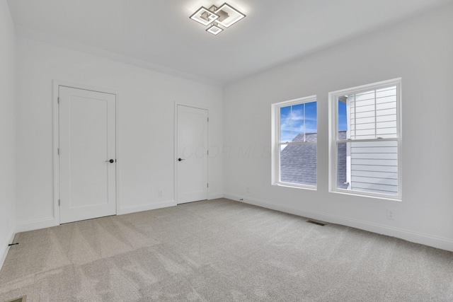 unfurnished bedroom featuring carpet floors, baseboards, multiple closets, and visible vents