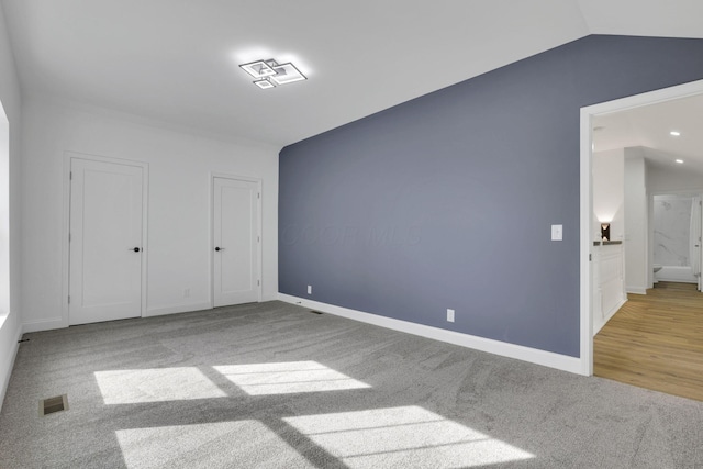 unfurnished bedroom with baseboards, visible vents, carpet, and vaulted ceiling