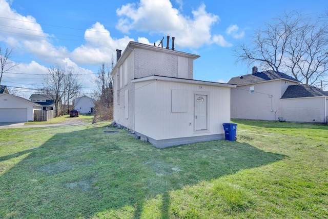 back of property featuring a chimney, a detached garage, an outdoor structure, and a lawn