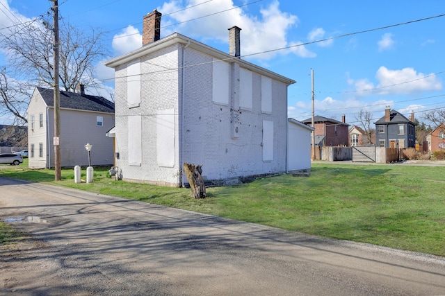 view of side of property featuring a lawn, a chimney, fence, brick siding, and a residential view