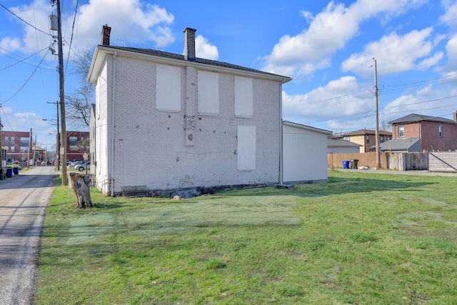 back of house featuring a yard, a chimney, fence, brick siding, and a residential view
