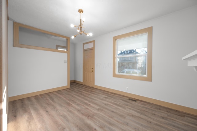 empty room with visible vents, wood finished floors, baseboards, and a chandelier