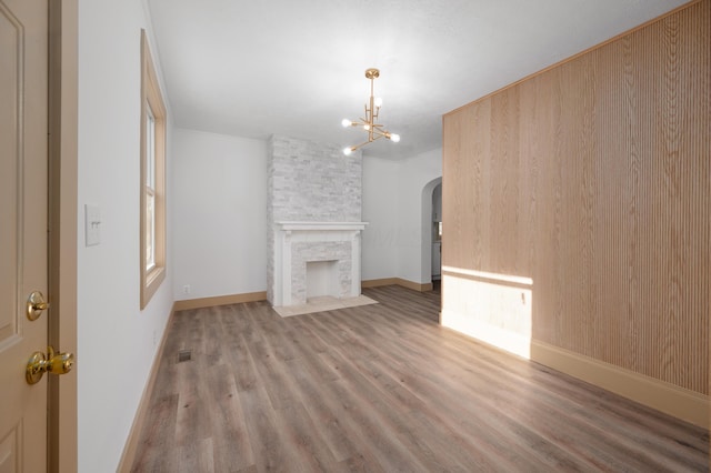 unfurnished living room featuring wood finished floors, baseboards, arched walkways, and a chandelier