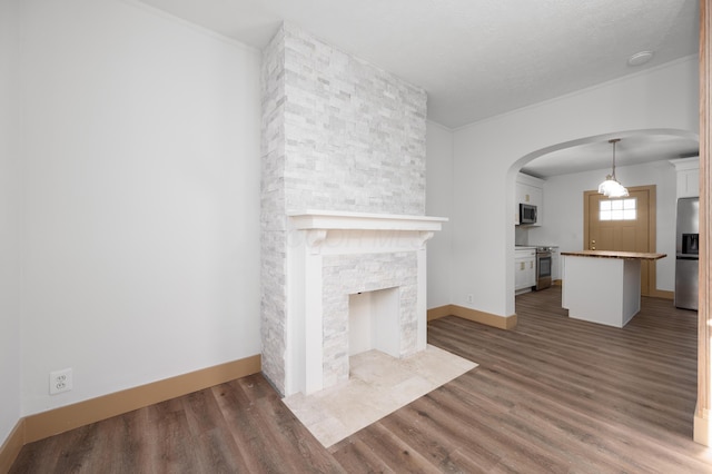 unfurnished living room with wood finished floors, crown molding, a fireplace, and arched walkways