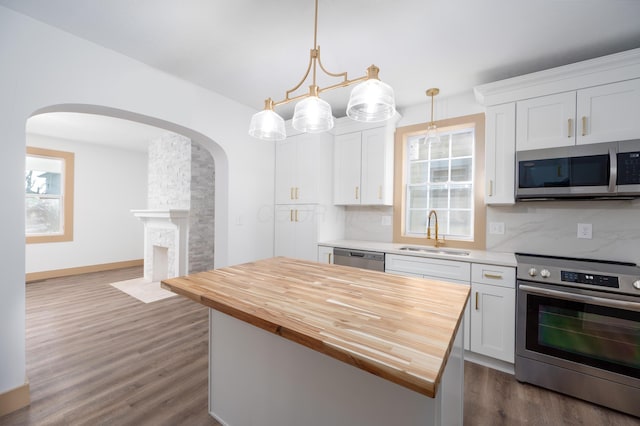 kitchen featuring backsplash, wooden counters, appliances with stainless steel finishes, arched walkways, and a sink