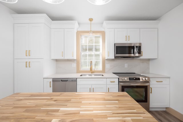 kitchen featuring a sink, decorative backsplash, stainless steel appliances, white cabinetry, and butcher block counters