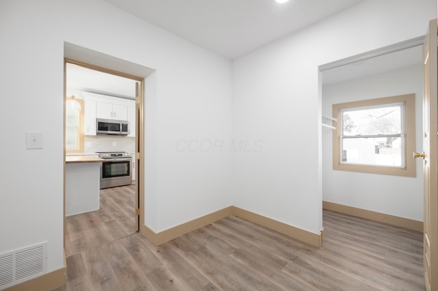 unfurnished room with light wood-type flooring, visible vents, and baseboards