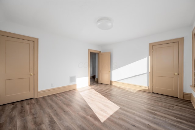 empty room featuring wood finished floors, visible vents, and baseboards
