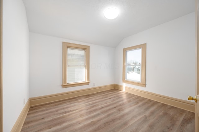 empty room with vaulted ceiling, wood finished floors, and baseboards