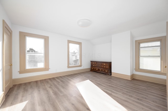 spare room featuring lofted ceiling, light wood-style floors, and baseboards