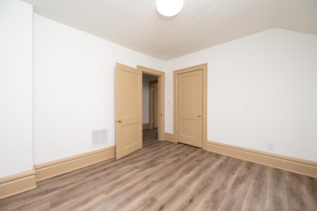 unfurnished room with visible vents, lofted ceiling, a textured ceiling, light wood-style floors, and baseboards