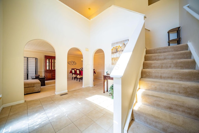 stairway featuring tile patterned flooring, crown molding, visible vents, high vaulted ceiling, and arched walkways