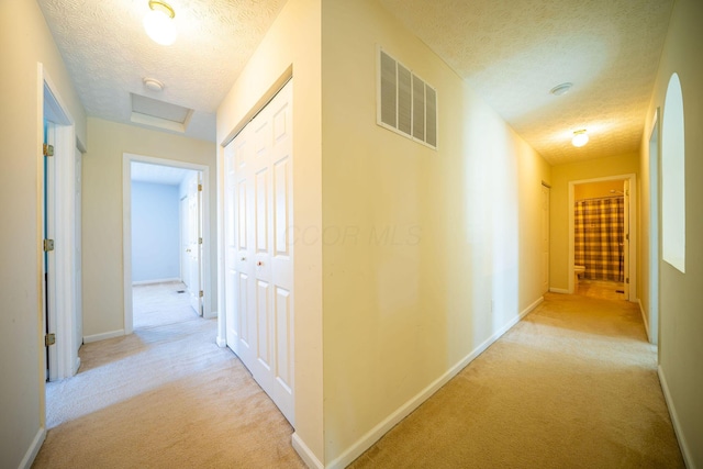 hallway with light carpet, visible vents, a textured ceiling, and baseboards