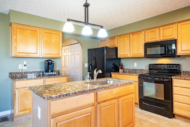 kitchen with light brown cabinetry, stone counters, a sink, and black appliances