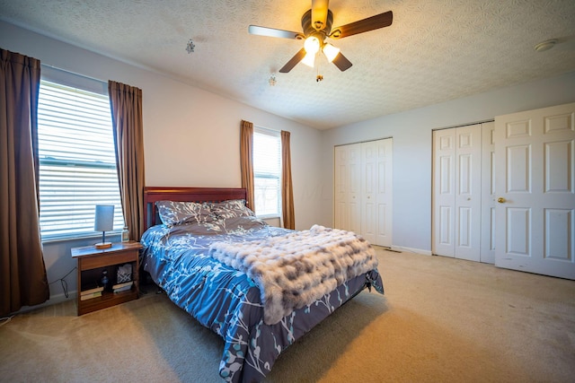 bedroom with carpet floors, a ceiling fan, two closets, and a textured ceiling