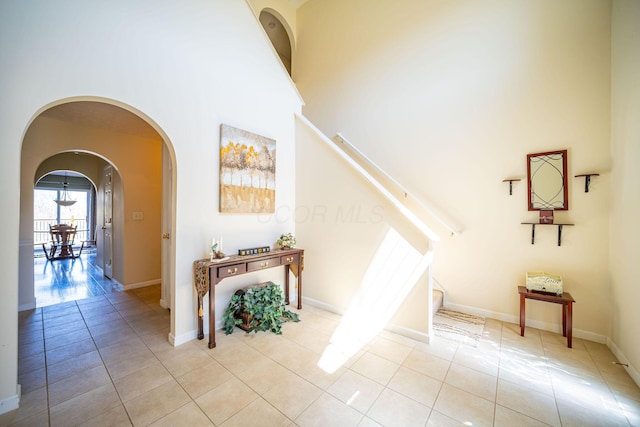 stairs with tile patterned floors, arched walkways, a high ceiling, and baseboards