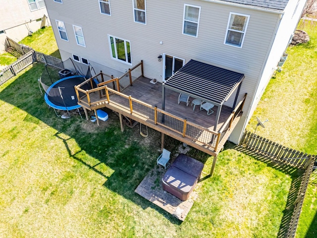 rear view of property with a trampoline, a deck, a fenced backyard, and a lawn