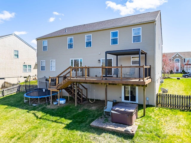 back of property with a hot tub, a yard, stairway, a trampoline, and a deck