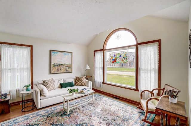 living area featuring vaulted ceiling, baseboards, a textured ceiling, visible vents, and wood finished floors