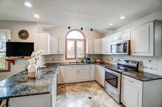 kitchen featuring white cabinets, stainless steel appliances, a sink, vaulted ceiling, and backsplash