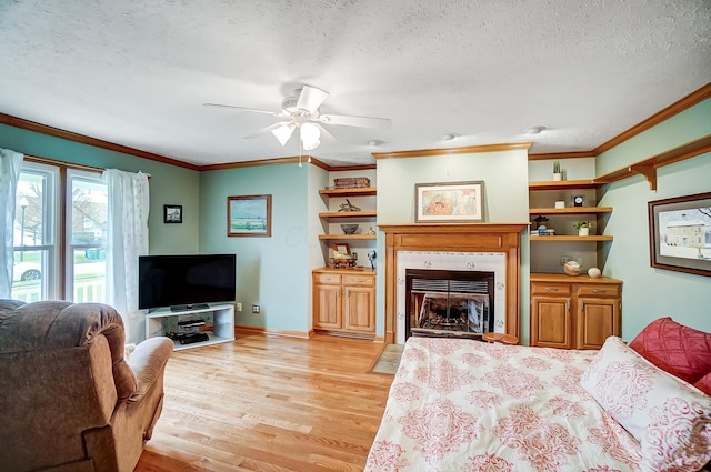 living area with light wood-type flooring, ornamental molding, a textured ceiling, ceiling fan, and a fireplace