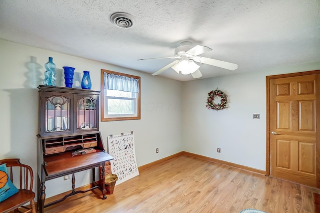 interior space featuring light wood-type flooring, baseboards, a textured ceiling, ceiling fan, and visible vents