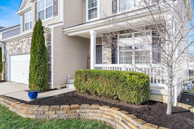 doorway to property featuring stone siding, driveway, a garage, and a porch