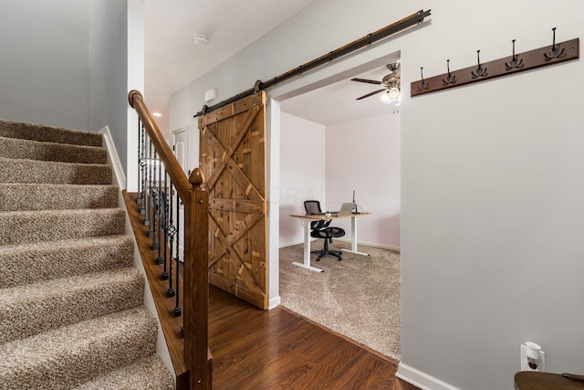 stairway with baseboards, a barn door, ceiling fan, and wood finished floors