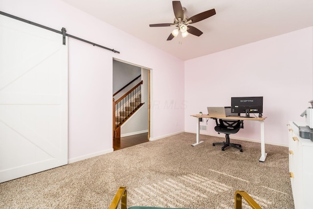office space with baseboards, a barn door, carpet, and a ceiling fan