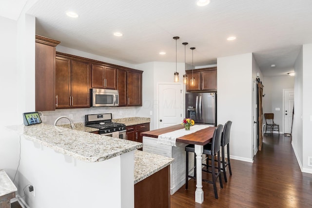 kitchen with a breakfast bar area, stainless steel appliances, dark wood-type flooring, backsplash, and a peninsula