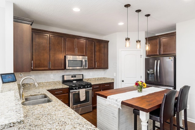 kitchen featuring light stone counters, dark brown cabinetry, a sink, tasteful backsplash, and appliances with stainless steel finishes