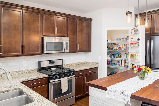 kitchen featuring tasteful backsplash, a sink, light stone counters, pendant lighting, and appliances with stainless steel finishes