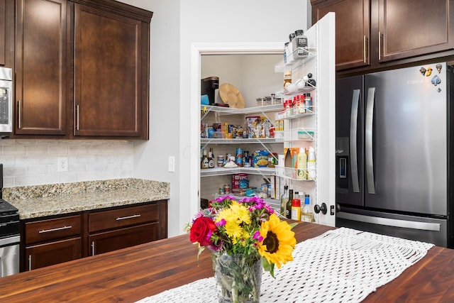 kitchen with dark brown cabinetry, stainless steel fridge, butcher block counters, and tasteful backsplash